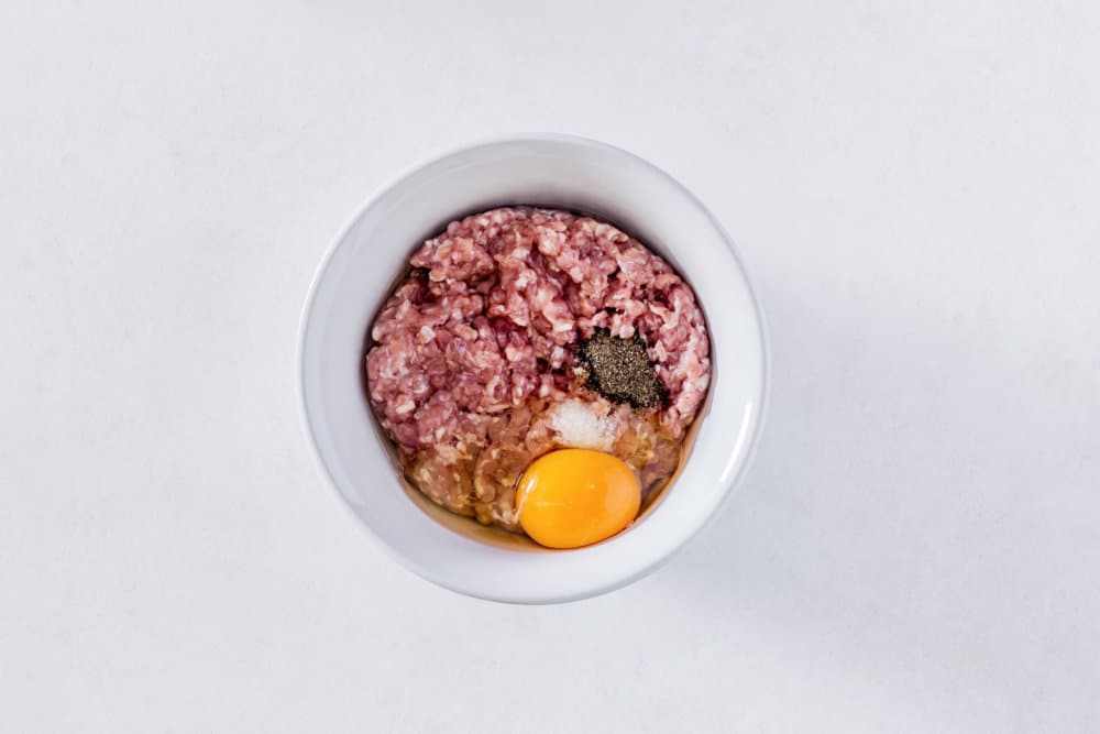 ground-meat-with-salt-and-pepper-and-an-egg-in-a-white-bowl