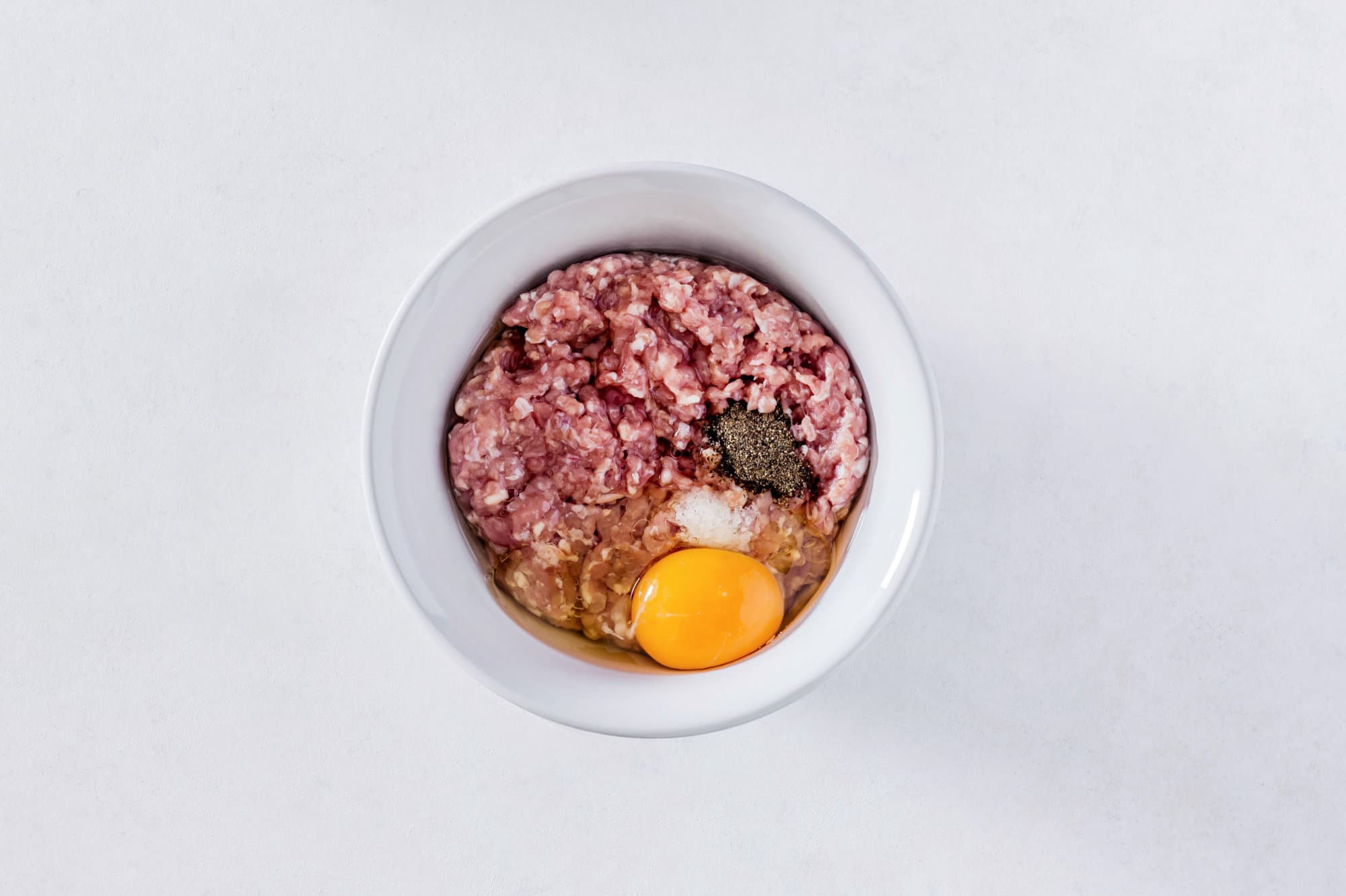 ground-meat-with-salt-and-pepper-and-an-egg-in-a-white-bowl