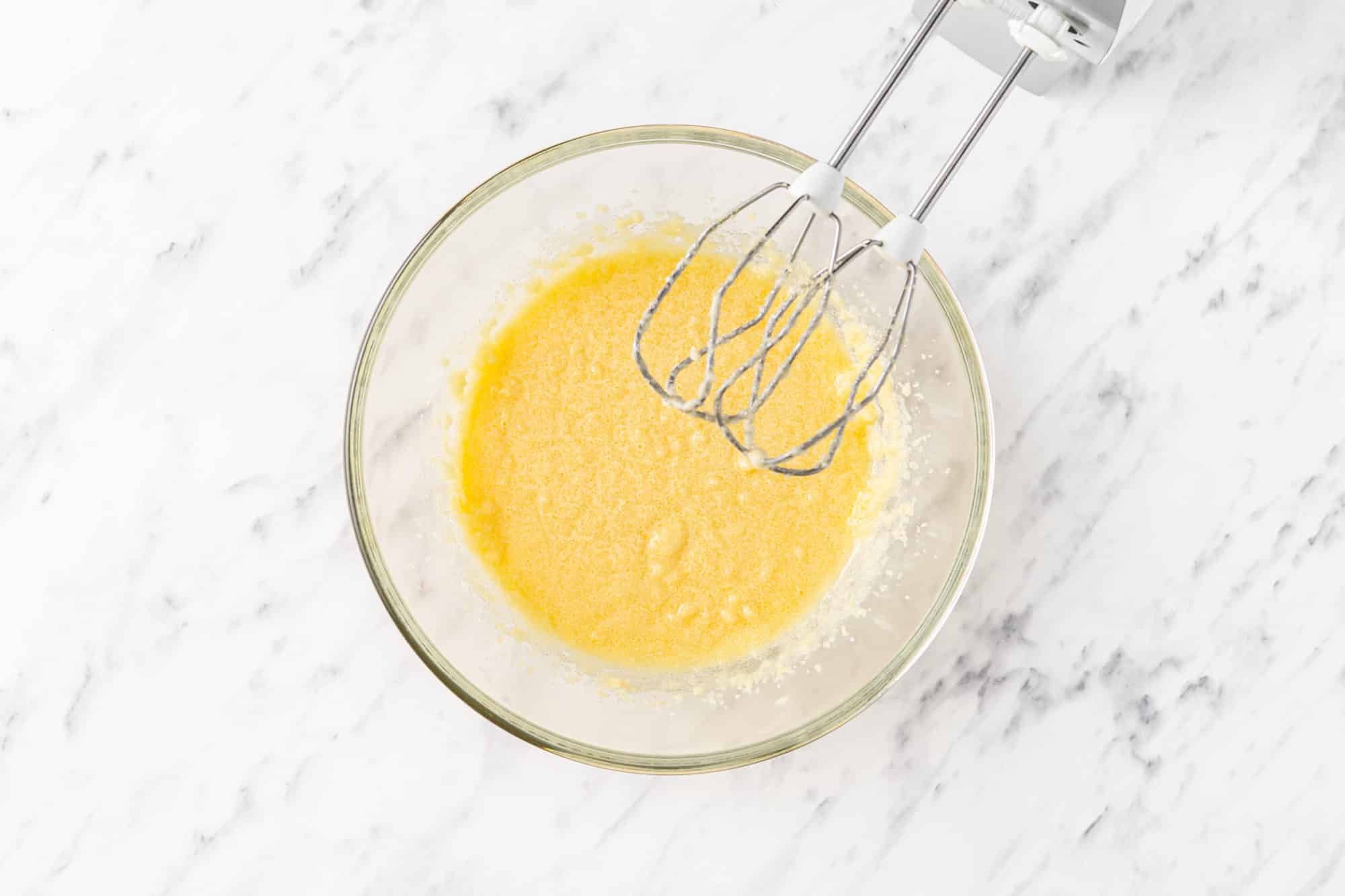 a glass bowl with an egg sugar mixture and hand mixers.