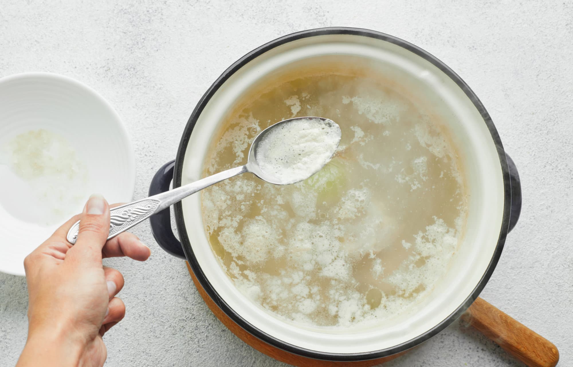 The BEST Chicken Noodle Soup Recipe (with Potatoes!) chicken-cooking-in-a-soup-pot-on-a-wooden-board-with-a-spoon-removing-the-foam-on-top