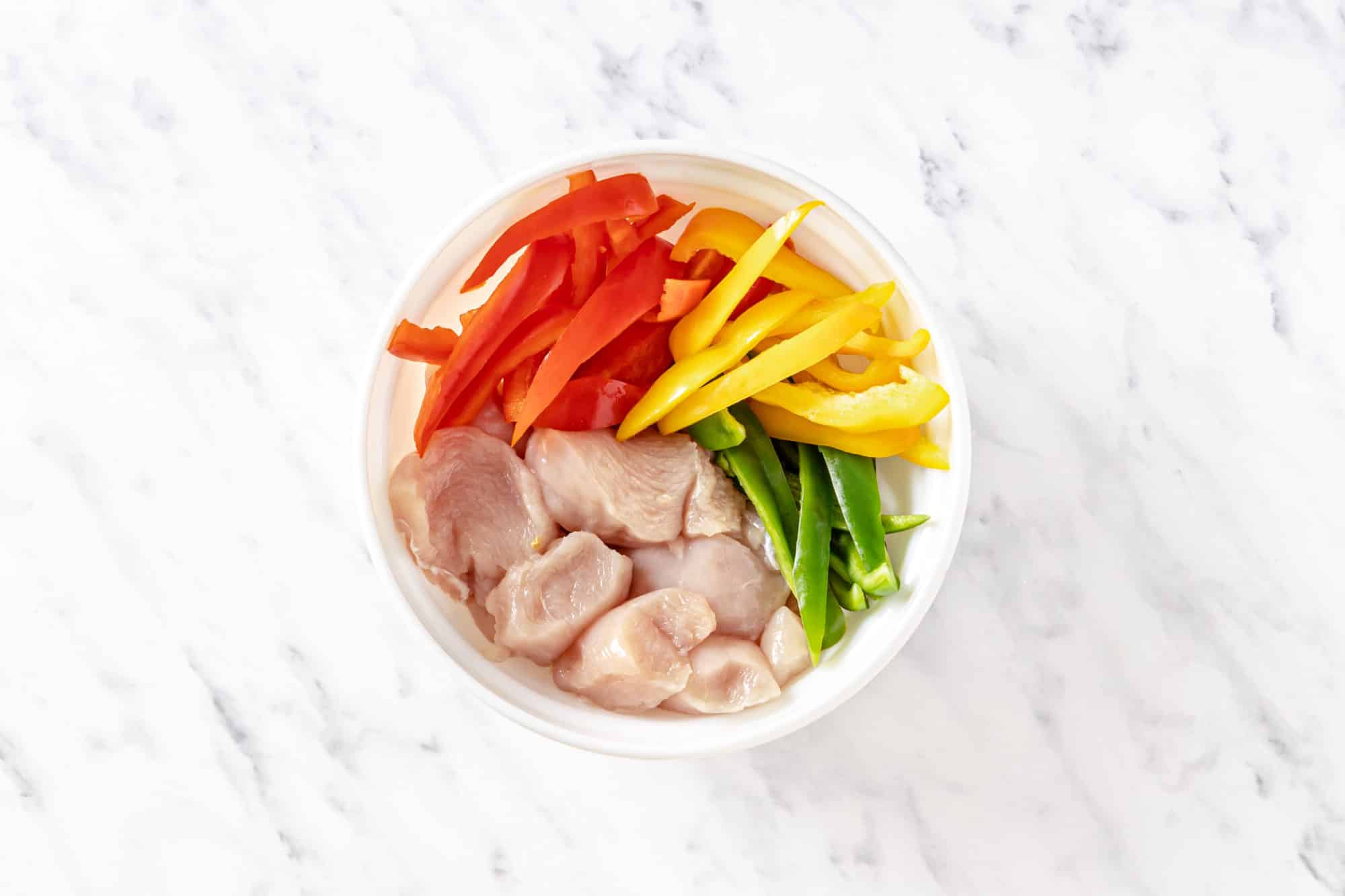 raw chopped veggies and chicken breast in a white bowl.