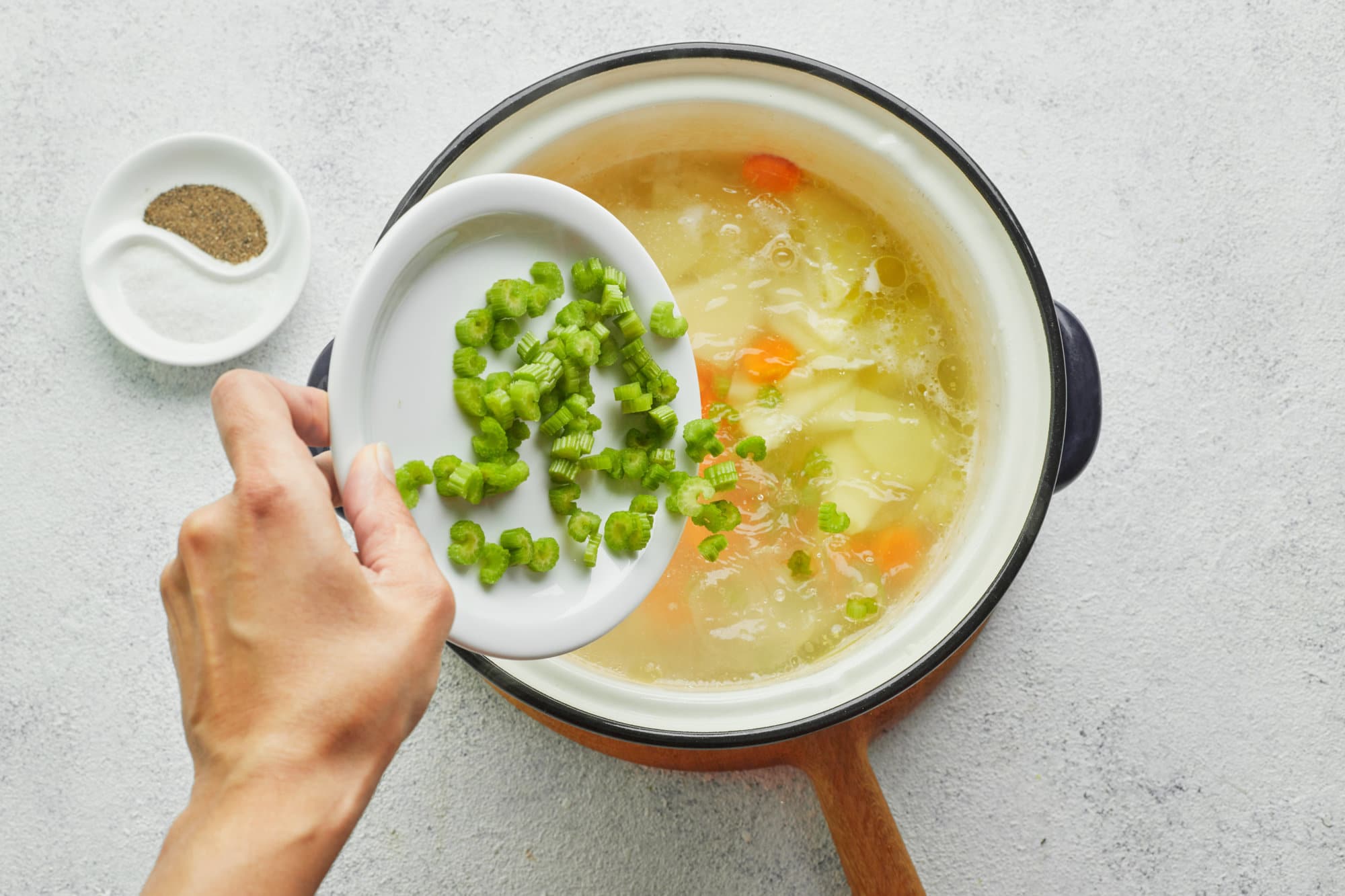 The BEST Chicken Noodle Soup Recipe (with Potatoes!) chicken-noodle-soup-in-a-soup-pot-on-a-wooden-board-with-green-onion-being-added-inside-with-a-bowl-of-salt-and-pepper-on-the-side