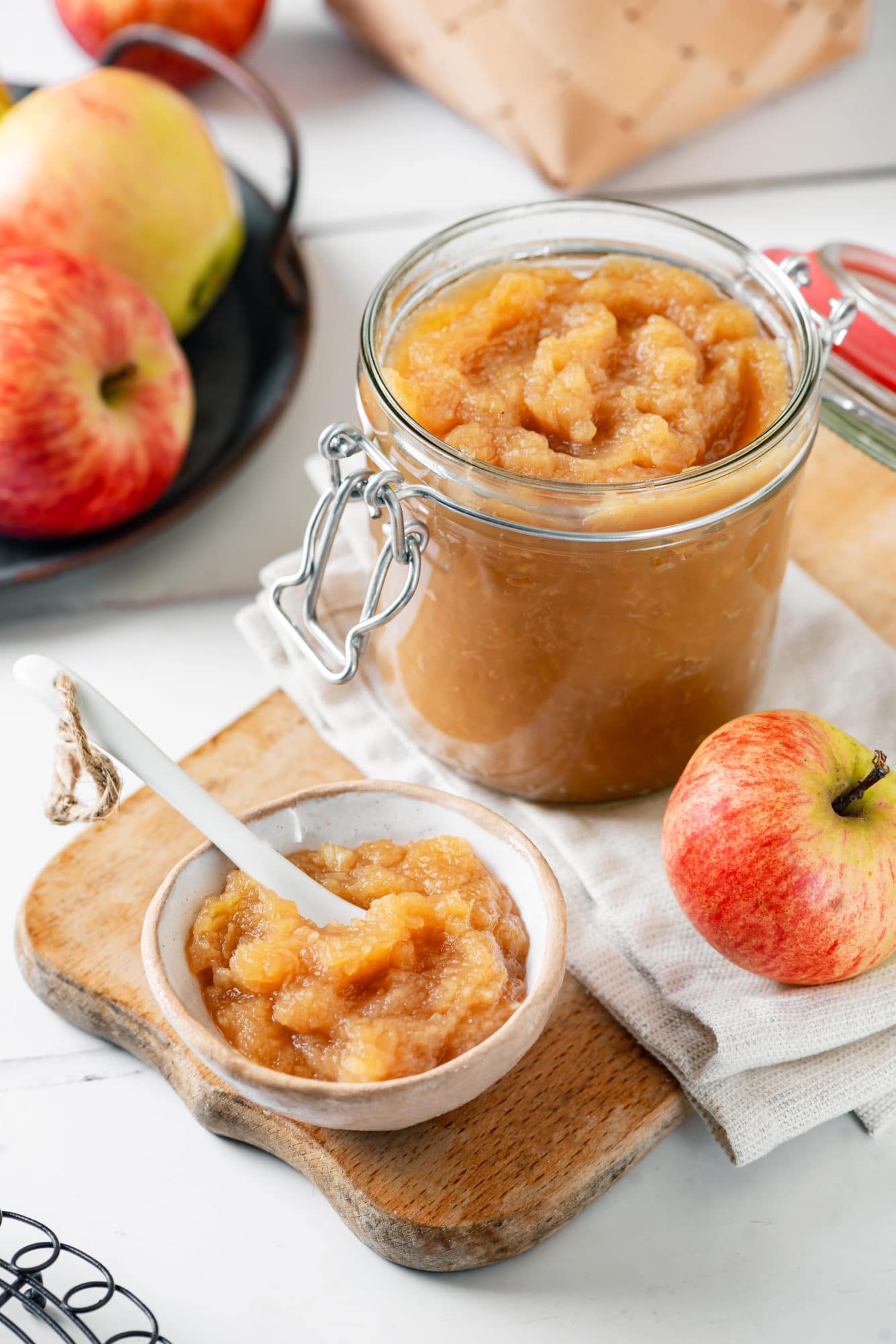 Easy Apple Jam with 2 Ingredients (homemade apple sauce) apple-jam-in-a-clear-jar-and-a-small-bowl-with-a-spoon-on-a-wooden-board-with-apples-on-the-side