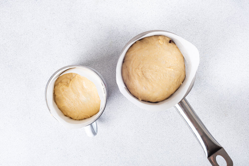 Easter bread dough in a sauce pan and mug with parchment paper.