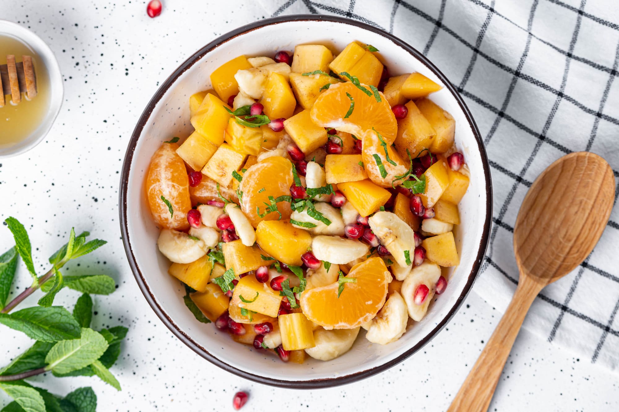 7 Desserts to Eat After Thanksgiving Dinner Persimmon fruit salad in a white bowl with a black rim and a towel on the side.