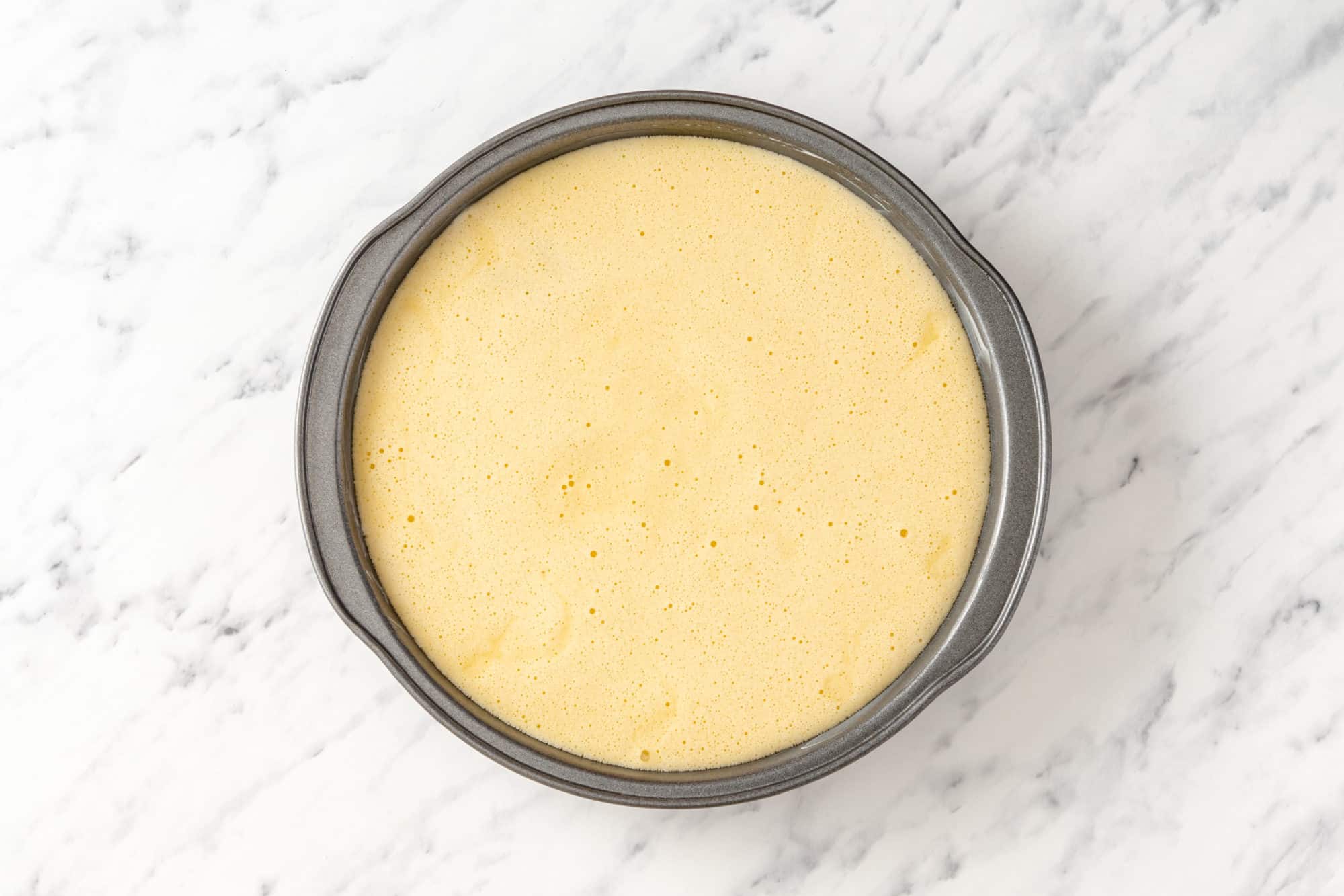 A grey 9-inch baking pan with cake batter poured in ready to bake.