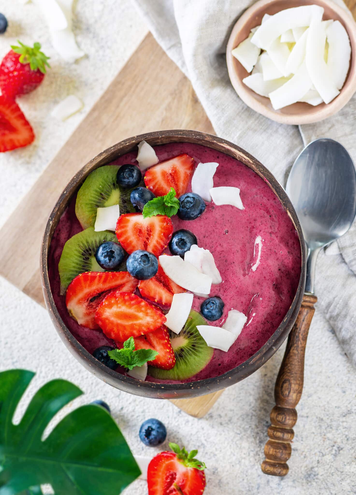 a purple acai smoothie bowl in a wooden bowl with a spoon on the side with fruit toppings on the smoothie bowl.