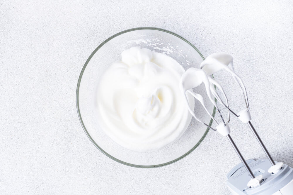White cream in a clear bowl and hand mixer for easter bread.