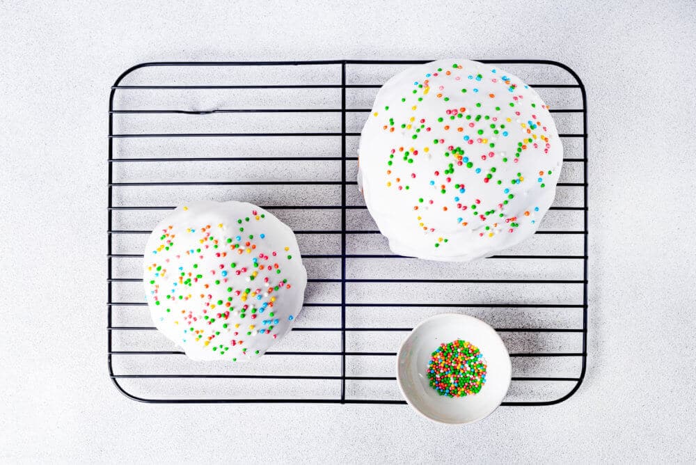 2 Easter breads with icing and sprinkles on a cooling rack.
