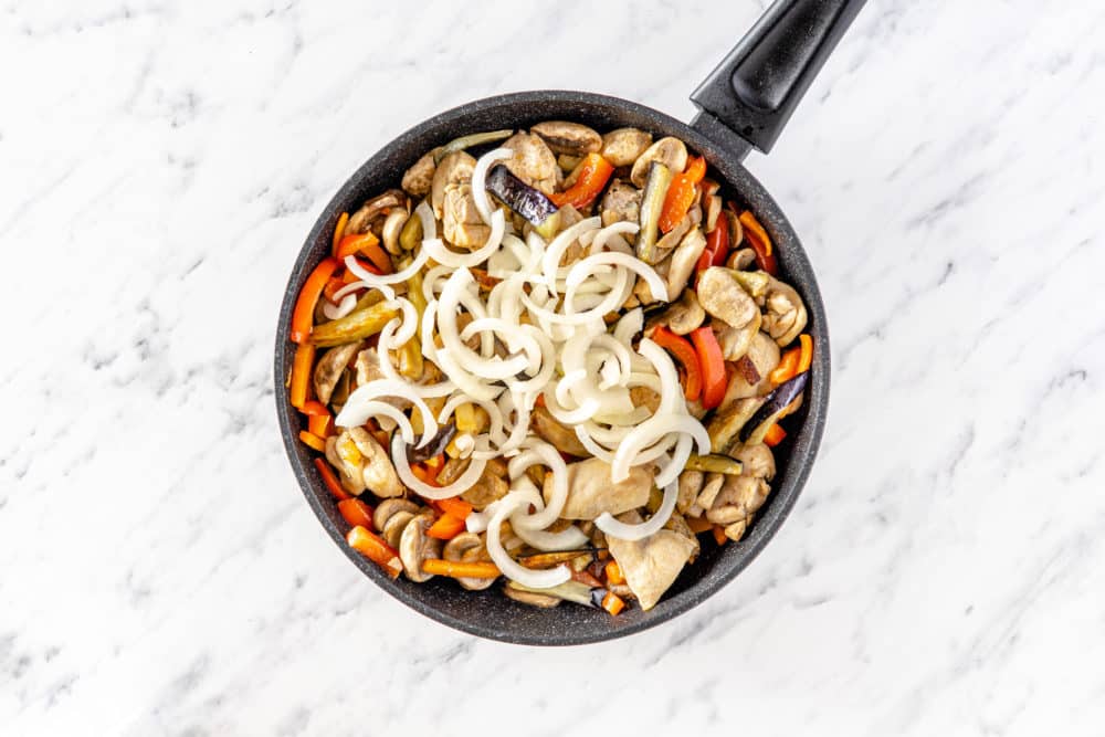 veggies with chicken in a pan with onion on top.