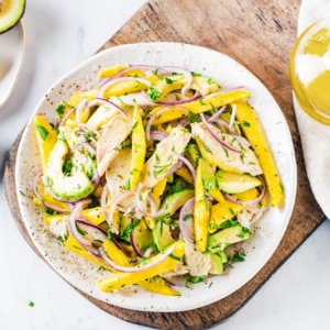 Easy Avocado and Chicken Salad with Mango Avocado and chicken salad with mango on a white plate on a wooden board.