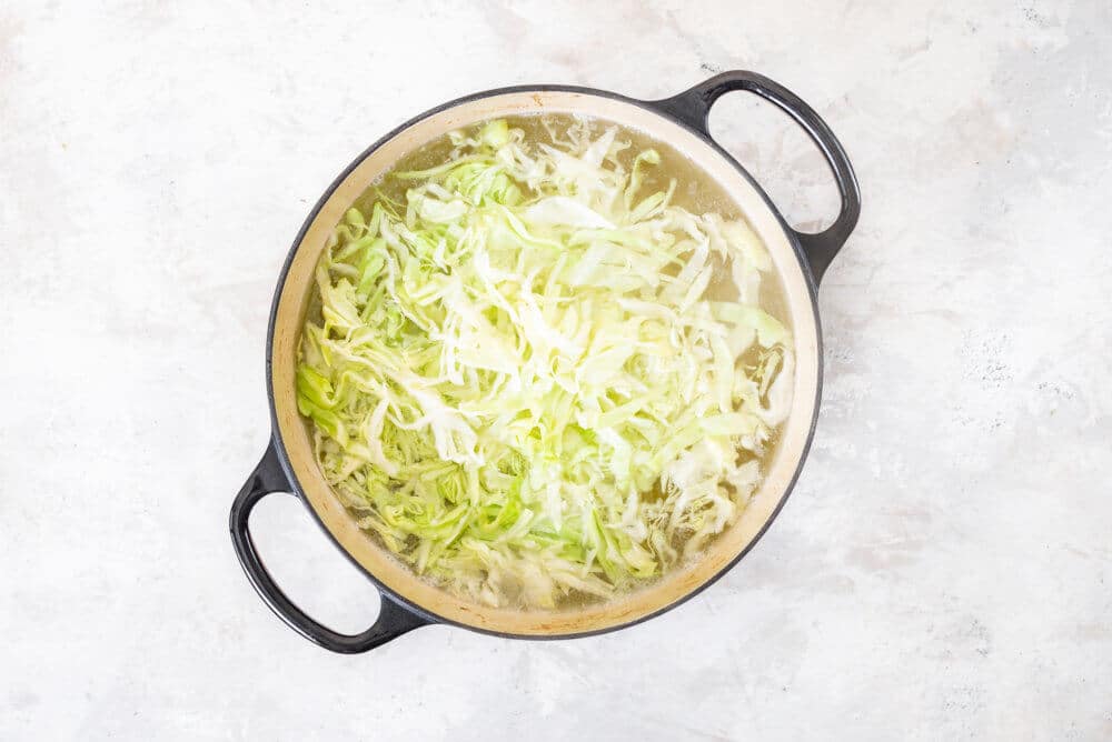 Cabbage and broth added to a soup pot.