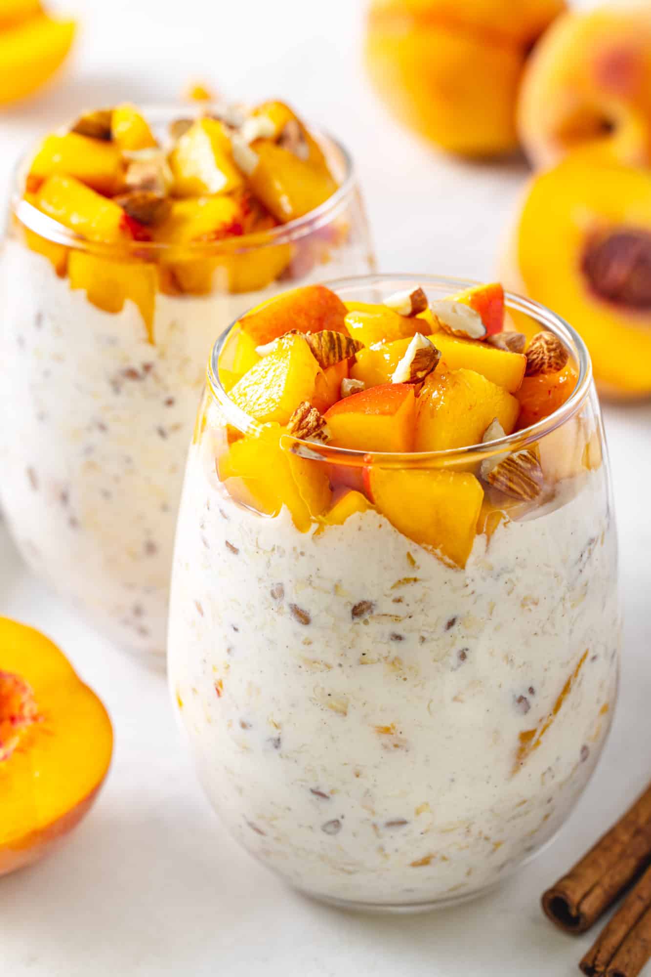 Peach Overnight Oats peach overnight oats on a marble board with whole peaches and cinnamon sticks seen in the background