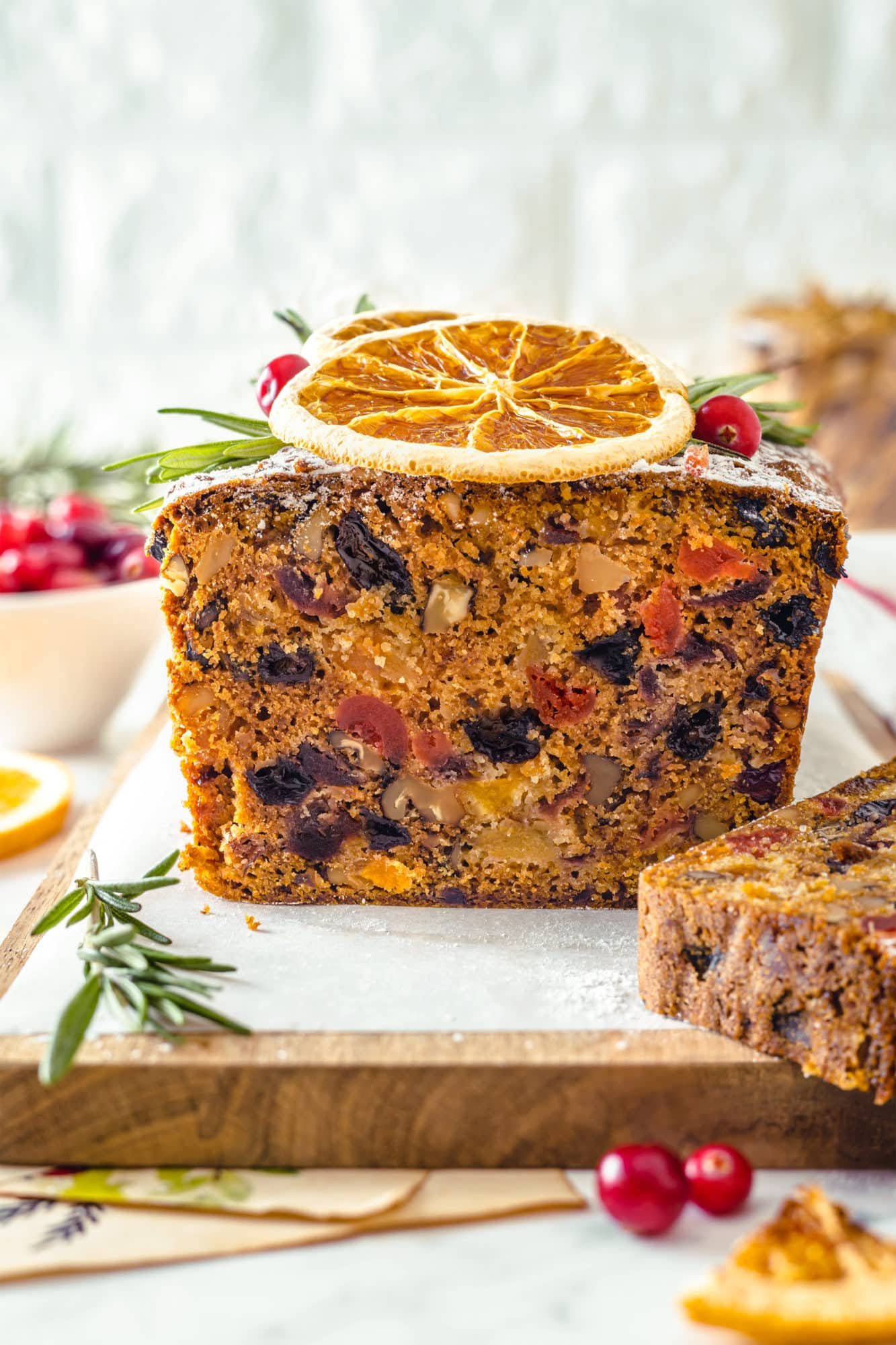 Christmas Fruit Cake with Brandy fruit cake side view of the baked inside on a wooden charcuterie board with a rosemary sprig on the side.