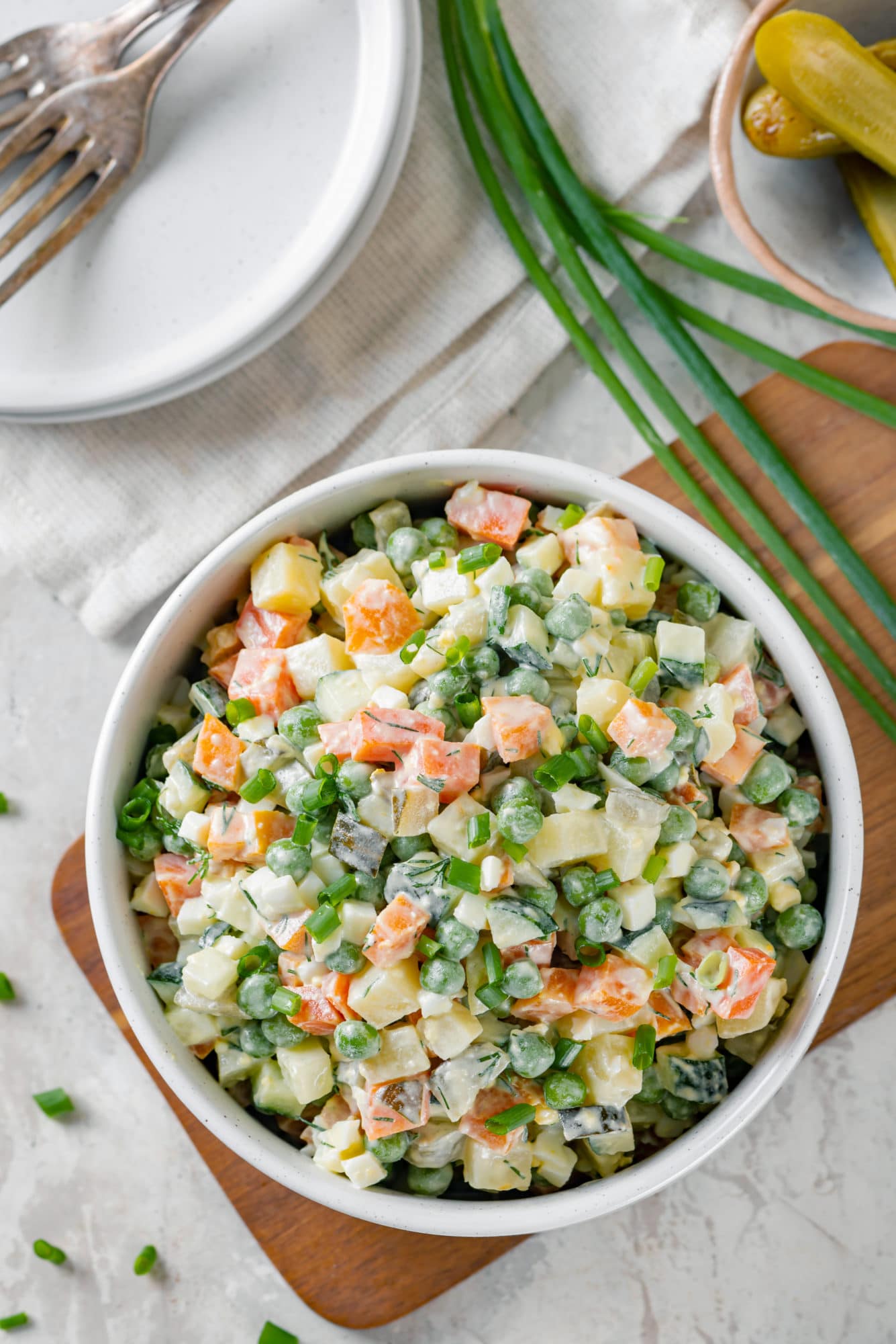 Simple and Classic Olivier Salad olivier-salad-in-a-white-bowl-on-a-wooden-board-with-green-onion