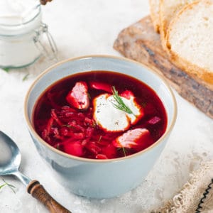 Simple and Classic Red Borscht A bowl of borscht with a dollop of sour cream on top with a spoon on the side.