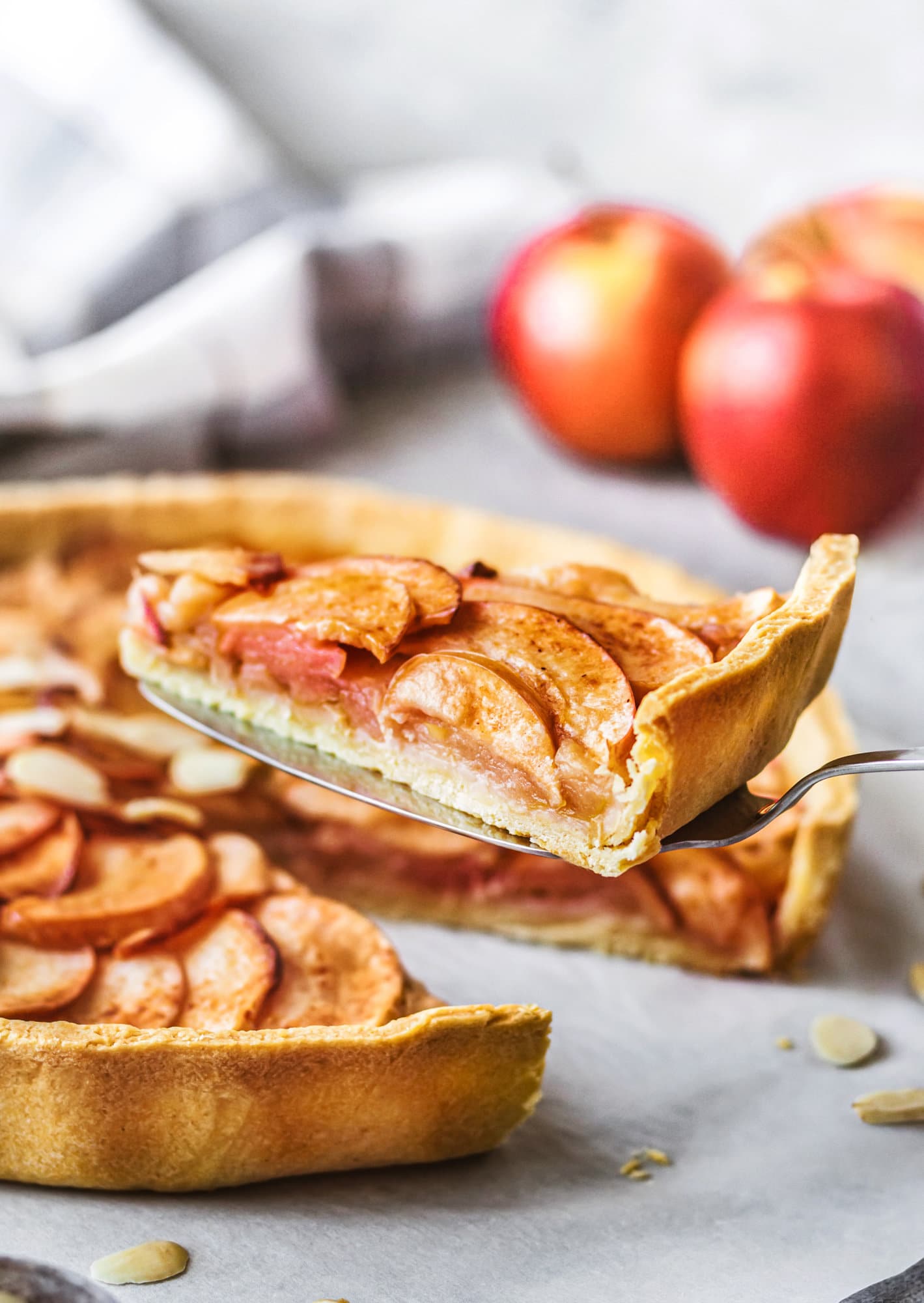 Baked Apple Tart with Cinnamon Apple tart slice picked up with a fork and apples in the background.