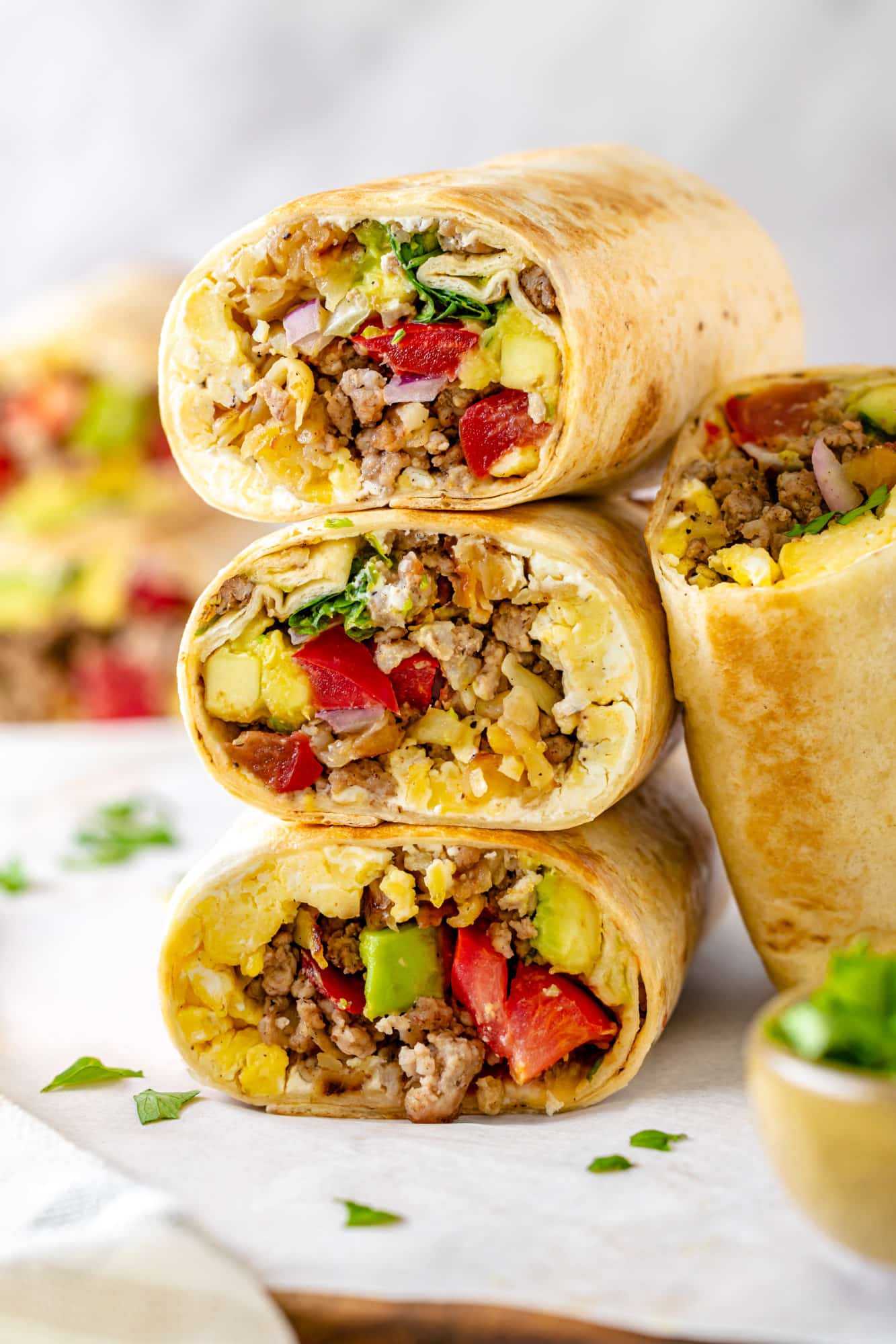 Homemade Breakfast Burritos with Potatoes A stack of breakfast burritos with another burrito half leaning on the side.