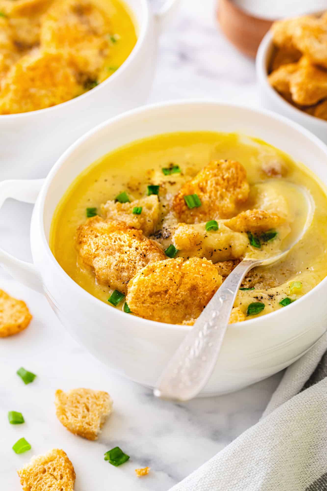 Simple One Pot Cauliflower Soup with Cheese a white bowl of creamy cauliflower soup with croutons and a spoon.