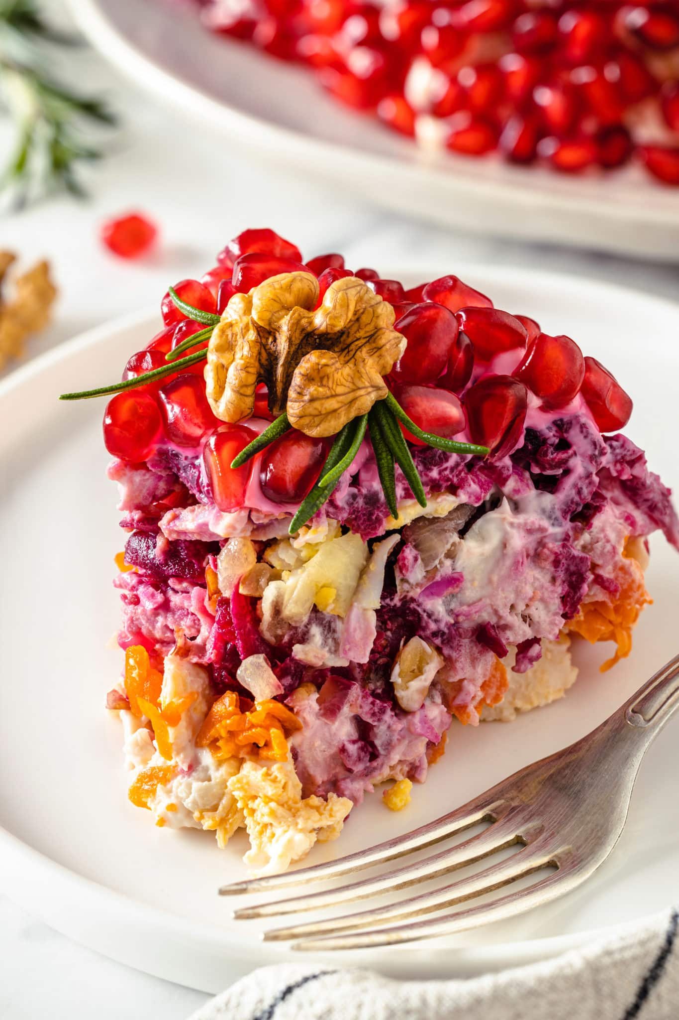 a piece of layered salad with a walnut and rosemary on top on a white plate with a fork.