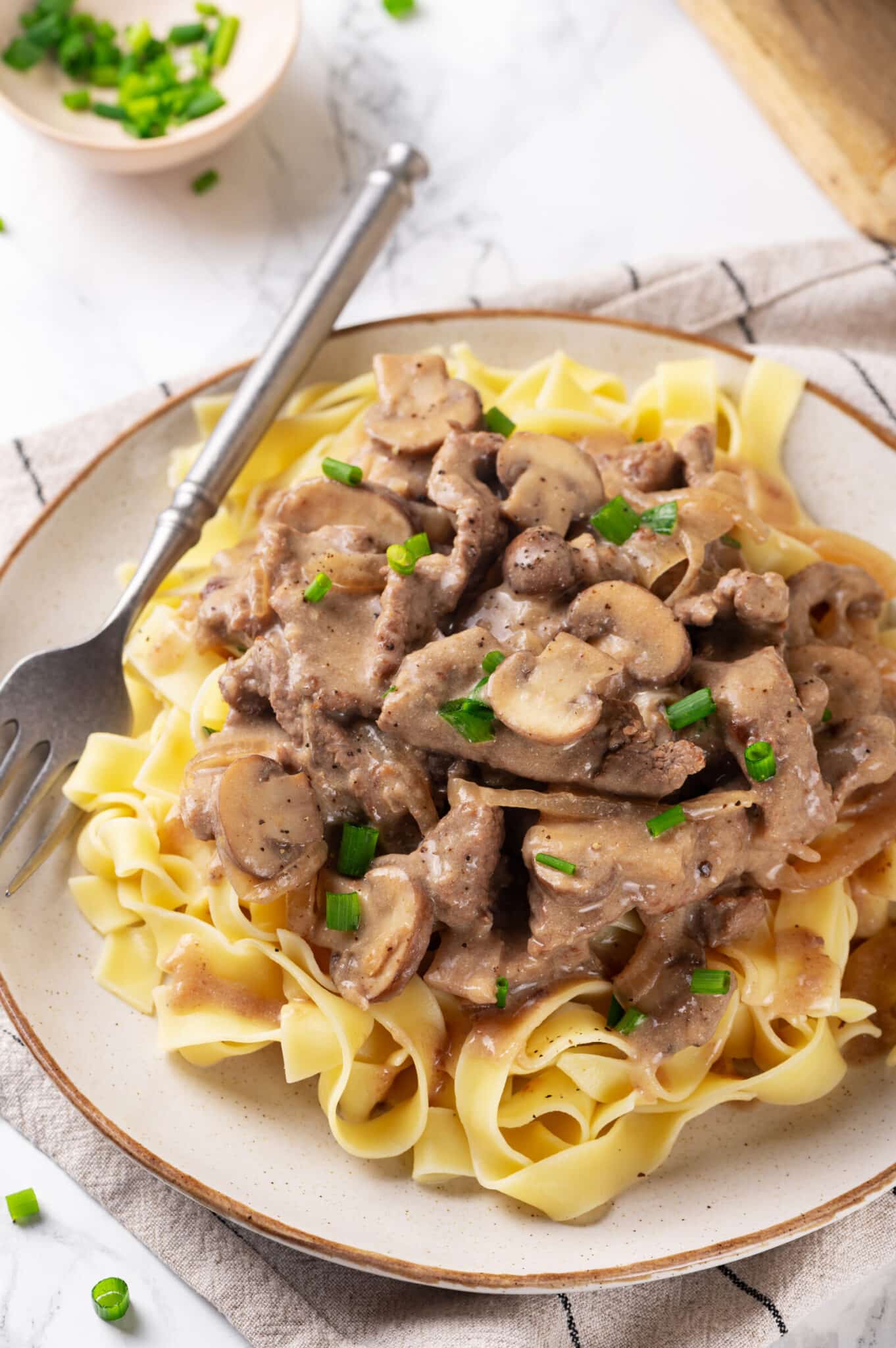 Easy Beef Stroganoff Recipe easy beef stroganoff with mushrooms served over egg noodles on a white plate with a fork beside it