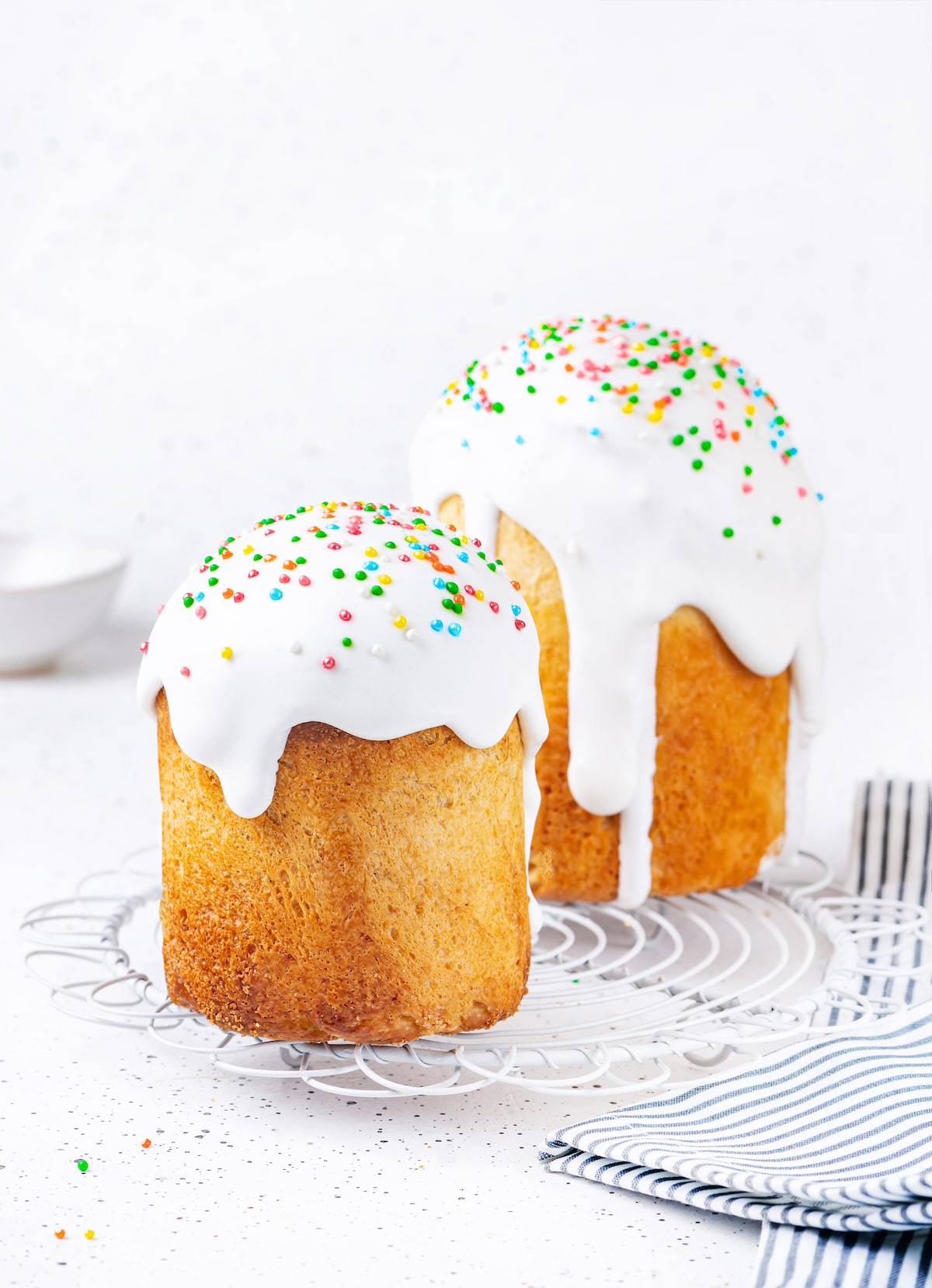 Easter Bread Machine Paska Recipe with Icing Easter bread soft bread with white icing dripping and topped with colorful sprinkles on white surface.