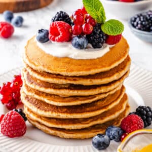 a stack of fluffy pancakes topped with cream and a selection of berries for garnish