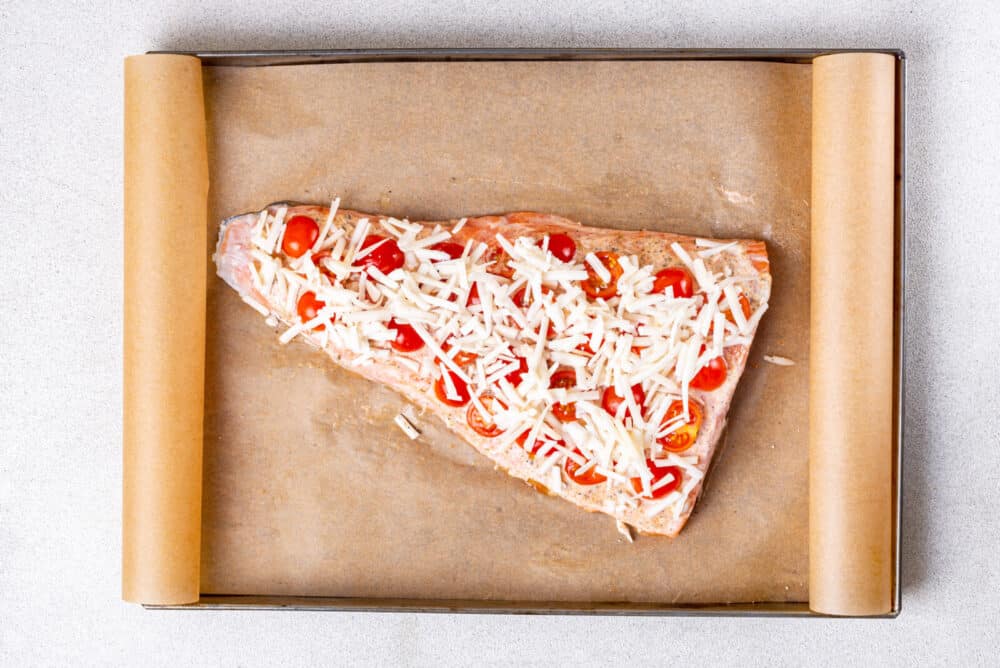 Ready to bake piece of salmon covered in tomatoes, seasoning, mayonnaise, and cheese.