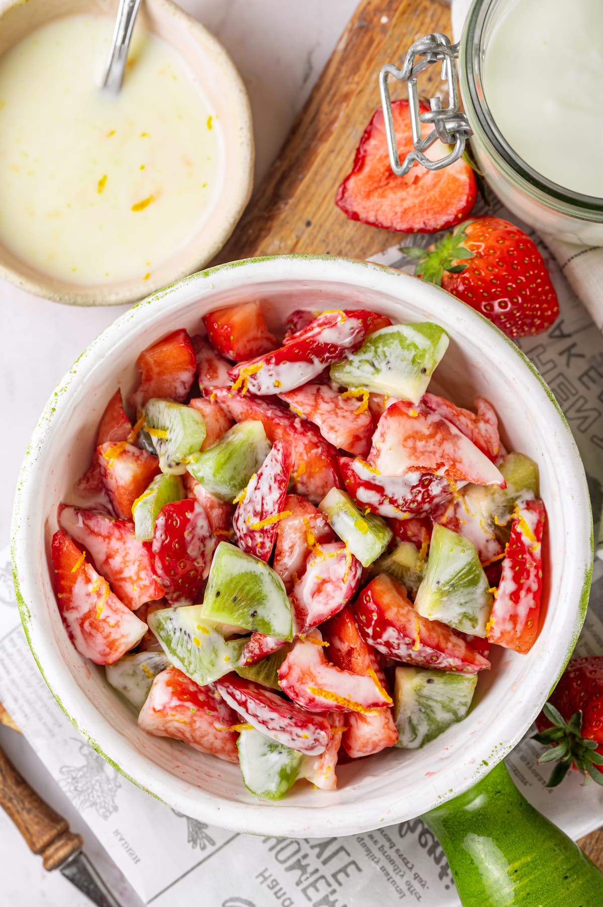 strawberry and kiwi salad with yogurt dressing in a dish with a green handle with more yogurt dressing on the side.